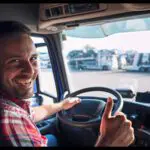 A man in plaid shirt sitting inside of a truck.