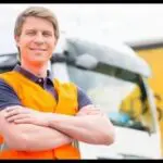 A man in an orange vest standing next to a truck.