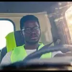 A man in safety vest driving a truck.