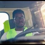 A man in safety vest driving a truck.